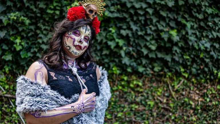 A woman in creative makeup and traditional costume for Dia de los Muertos, photographed outdoors.